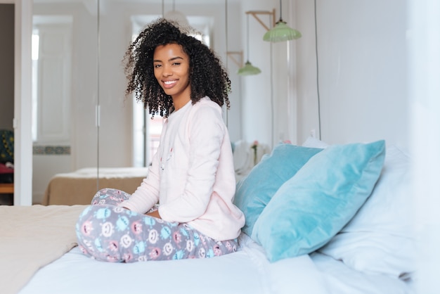 Heureuse belle jeune femme noire détendue assis dans le lit