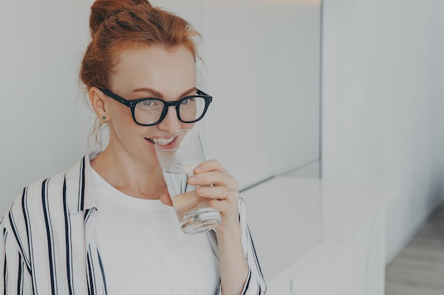 Heureuse belle jeune femme rousse en bonne santé buvant de l'eau le matin à la maison