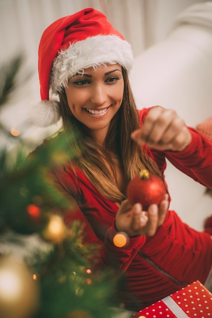 Heureuse belle jeune femme tenant un ornement de Noël rouge. Elle décore le sapin de Noël à la maison. Mise au point sélective.