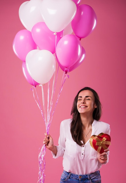 Heureuse belle jolie jolie femme avec des ballons colorés et un cadeau dans les mains, c'est s'amuser et célébrer. Anniversaire, vacances, Saint Valentin et autres