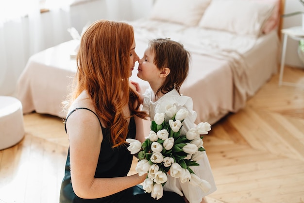 Heureuse belle mère affectueuse avec un bouquet de fleurs printanières embrasse sa fille à la maison sur le lit profite du moment de surprise célèbre la fête des mères