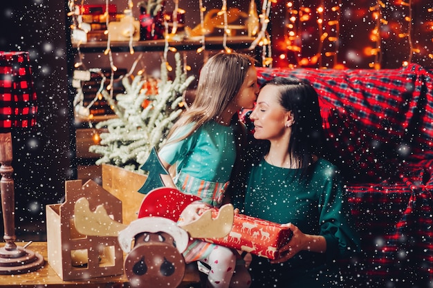 Heureuse et belle mère avec sa jolie fille fêtant Noël à la maison, se présentant, s'embrassant et s'embrassant.