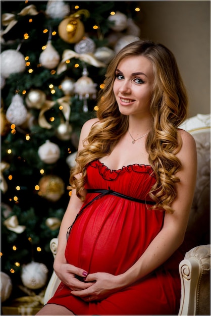heureuse blonde enceinte dans un peignoir rouge posant sur fond d'arbre de noël.
