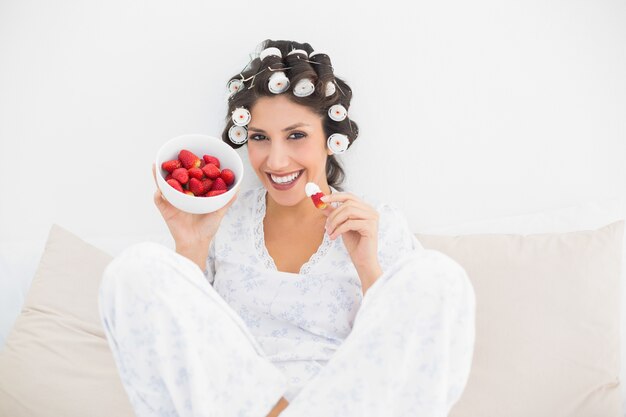 Heureuse brune en bigoudis avec un bol de fraises