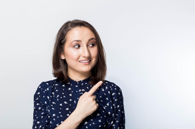 Heureuse charmante jeune femme montrant un doigt et pointant vers le haut sur fond blanc. Fille présente vos produits