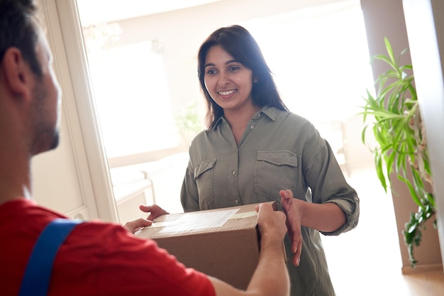 Heureuse cliente indienne recevant une boîte de livraison par courrier debout à la maison