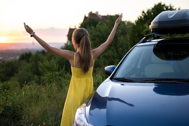 Heureuse conductrice en robe d'été profitant d'une soirée chaude près de sa voiture Concept de voyage et de vacances