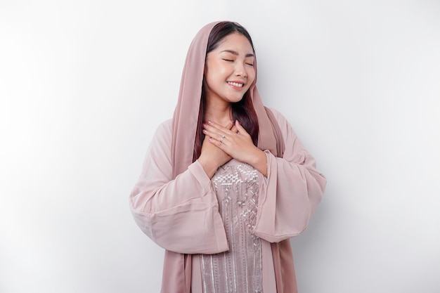 Heureuse consciente reconnaissante jeune femme musulmane asiatique avec sa main sur sa poitrine souriant isolé sur fond blanc