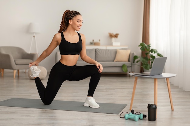 Heureuse dame africaine faisant des exercices de hanche et de jambe à la maison