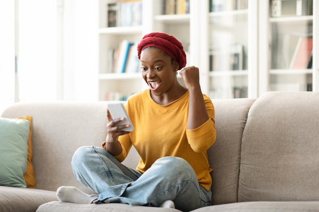 Heureuse dame africaine utilisant le téléphone et levant le poing