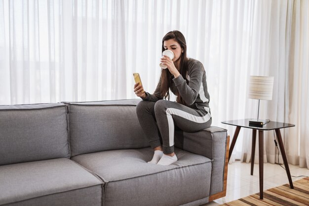 Heureuse dame latine se détendre en buvant du café à la maison seule s'asseoir dans la chambre pose partager de bonnes nouvelles