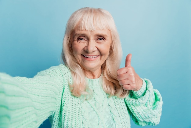 Heureuse dame mûre joyeuse prenant selfie montrer beau signe de pouce isolé sur fond bleu