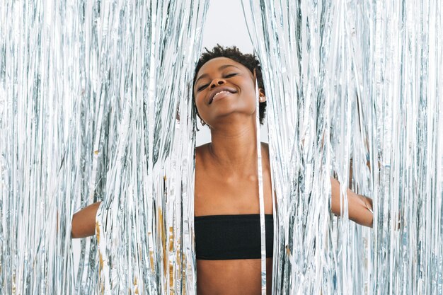 Heureuse danse jeune femme afro-américaine en haut noir sur fond argenté scintillant