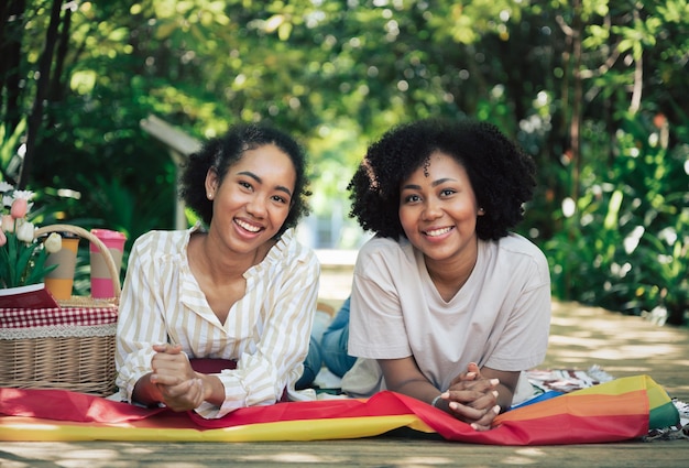 Heureuse deux femmes se couchent avec le drapeau LGBT dans le jardin