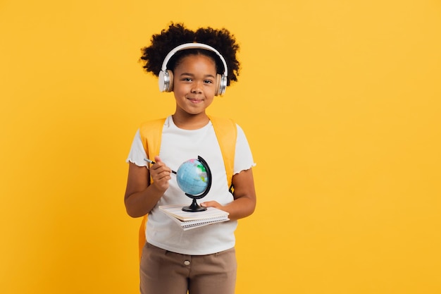 Heureuse écolière afro-américaine dans un casque avec sac à dos regardant l'espace de copie du globe géographique