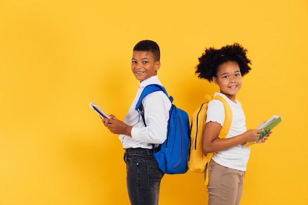 Heureuse écolière afro-américaine et écolier métis tenant des livres côte à côte sur fond jaune Concept de retour à l'école