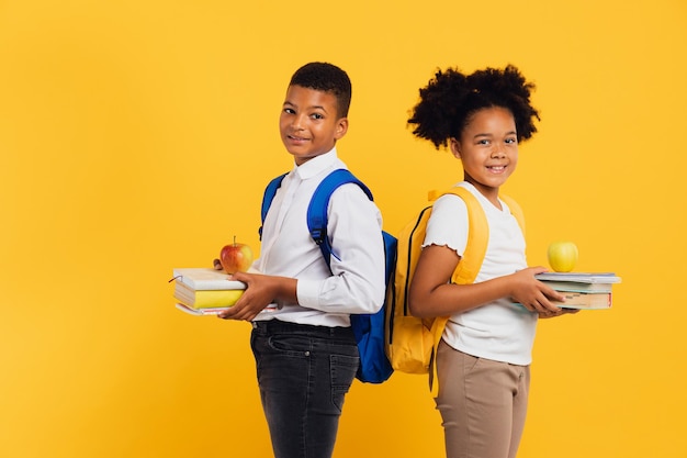 Heureuse écolière afro-américaine et écolier métis tenant des livres côte à côte sur fond jaune Concept de retour à l'école