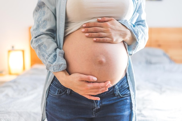 Heureuse enceinte en jeans bleu mère étreint son ventre nu se bouchent