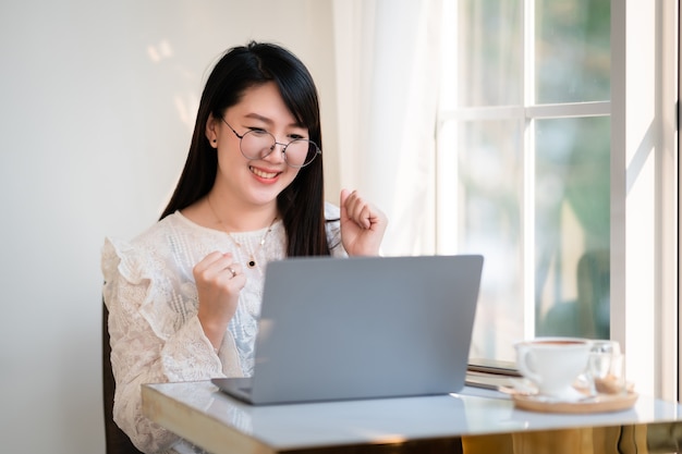 Heureuse entreprise prospère de femmes d'affaires indépendantes asiatiques a exprimé sa confiance enhardie à travailler avec un ordinateur portable assis dans un café comme l'arrière-plan, concept de communication