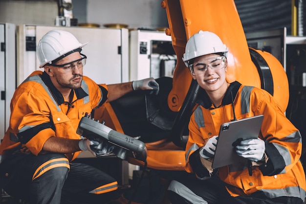 Heureuse équipe d'ingénieurs travaillant dans une usine d'automatisation moderne avec une opération de formation au contrôle du bras du robot de soudage ouvrière technologie de l'industrie de l'apprentissage automatique