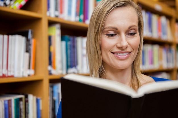 Heureuse étudiante en lisant un livre dans la bibliothèque de l&#39;université