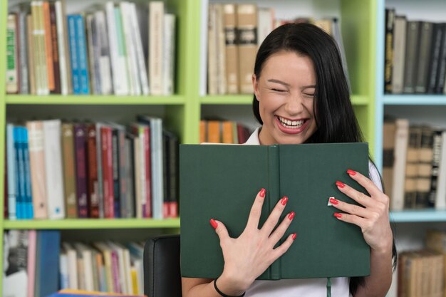 Heureuse étudiante lisant un livre dans la bibliothèque