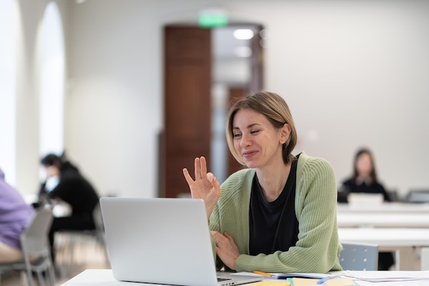 Heureuse étudiante mature montrant un geste ok pendant une classe virtuelle étudiant en ligne dans la bibliothèque