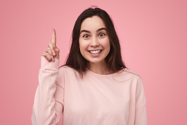 Heureuse étudiante pointant vers le haut et souriant à la caméra