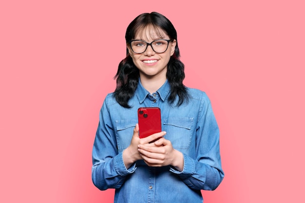 Heureuse étudiante avec smartphone sur fond rose