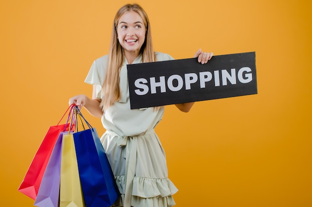 Heureuse excitée jolie jeune femme avec signe de shopping et de sacs colorés isolés sur jaune