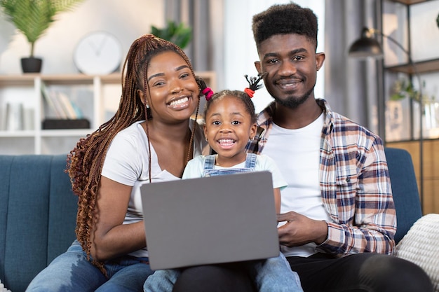 Heureuse famille africaine utilisant un ordinateur portable assis sur un canapé