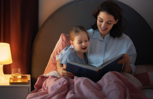 Heureuse famille aimante. Jolie jeune mère lisant un livre à sa fille sur le lit à la maison.