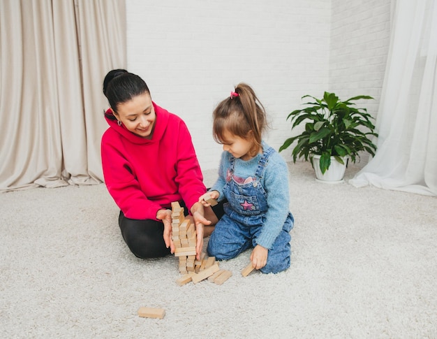 Heureuse famille aimante jouant avec des blocs de bois et s'amusant. Mère et sa fille fille jouant ensemble.