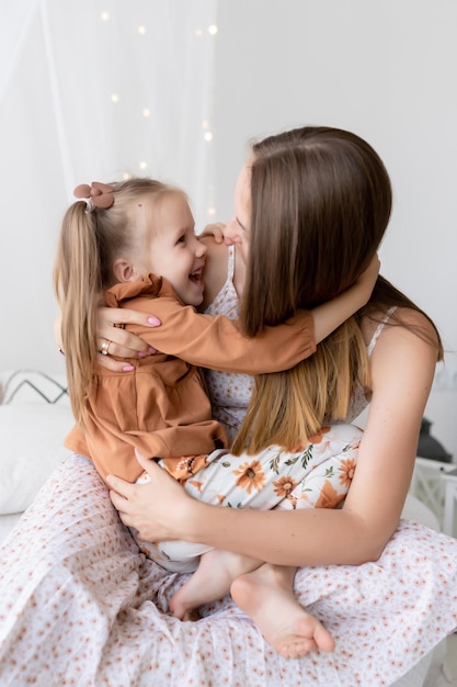 Heureuse famille aimante Mère et sa fille jouent et s'amusent sur le lit dans la chambre Ils sourient et se regardent Le plaisir d'être maman félicitations pour la fête des mères