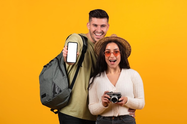 Heureuse famille arabe millénaire surprise avec la bouche ouverte dans des lunettes sac à dos montrer téléphone avec écran vide