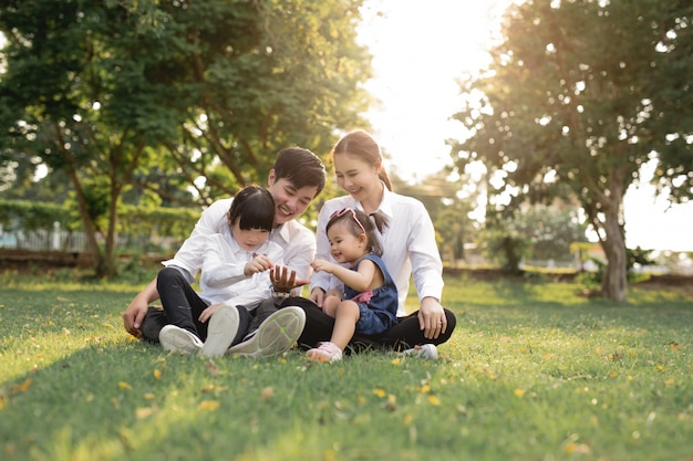 Heureuse Famille Asiatique Assise Sur L'herbe, Les Parents Avec Deux Enfants Sourient.