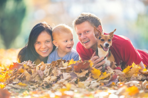 Heureuse famille mère père bébé garçon et chien dans le parc en automne jouant avec des feuilles.