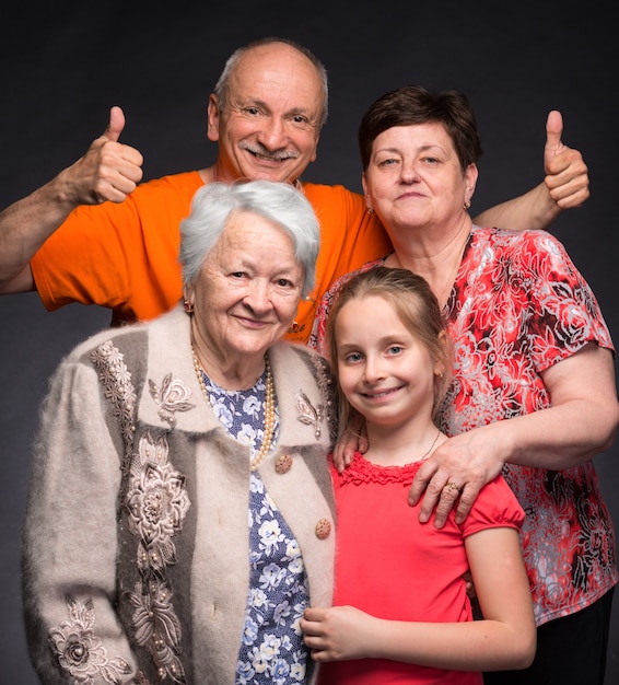 Heureuse famille multi-génération qui pose en studio sur un mur gris