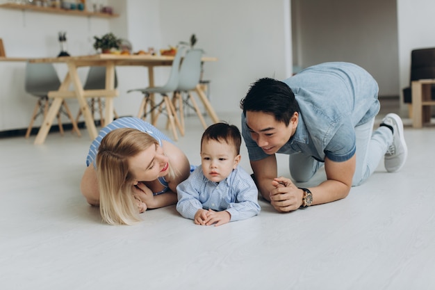 Heureuse famille multiculturelle s'amuser ensemble dans la cuisine. Papa asiatique et maman caucasienne apprennent à leur fils à ramper