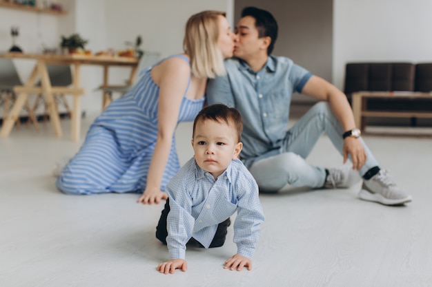 Heureuse famille multiculturelle s'amuser ensemble dans la cuisine. Papa asiatique et maman caucasienne apprennent à leur fils à ramper