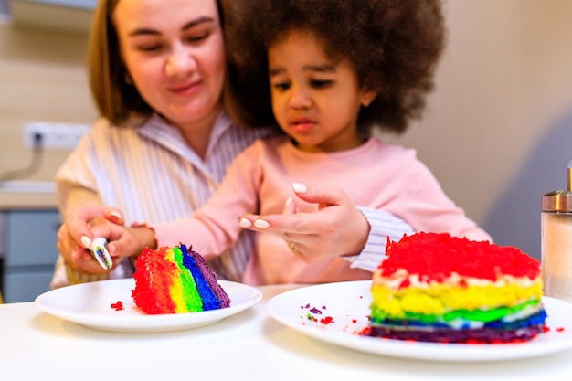 Heureuse famille multiethnique mangeant un gâteau arc-en-ciel à la cuisine