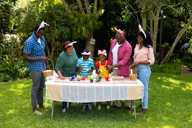 Heureuse famille multigénérationnelle afro-américaine dans des oreilles de lapin peignant des oeufs de pâques dans l'arrière-cour