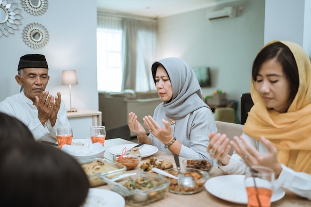 Heureuse famille musulmane asiatique priant avant d'avoir leur repas iftar pendant le jeûne du ramadan