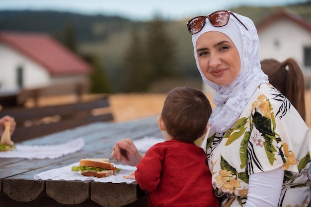 Heureuse famille musulmane mangeant à une table dans le parc tout en pique-niquant pendant les vacances d'été