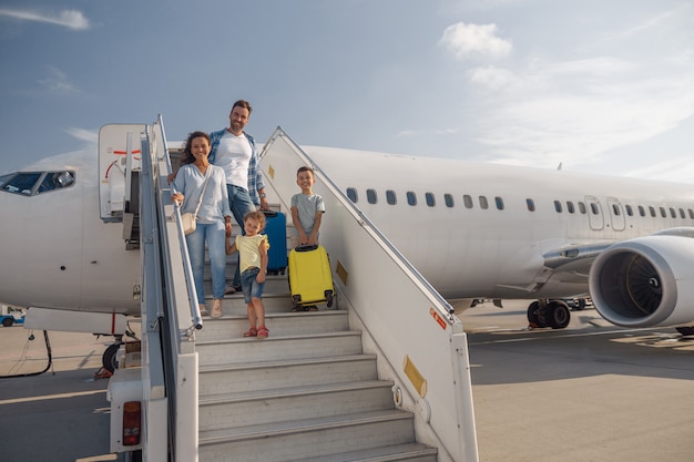 Heureuse famille de quatre personnes descendant de l'avion un jour. Les gens, les voyages, le concept de vacances