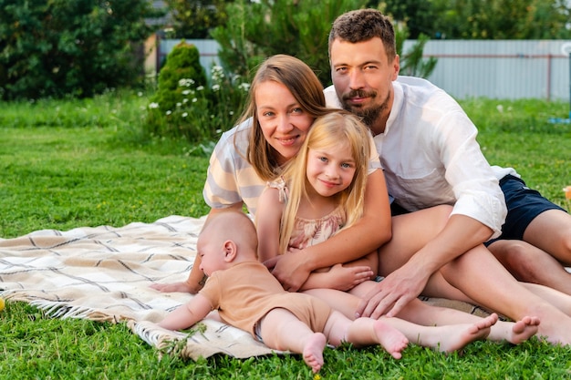 Heureuse famille de quatre personnes s'amusant ensemble en se reposant sur une couverture en été