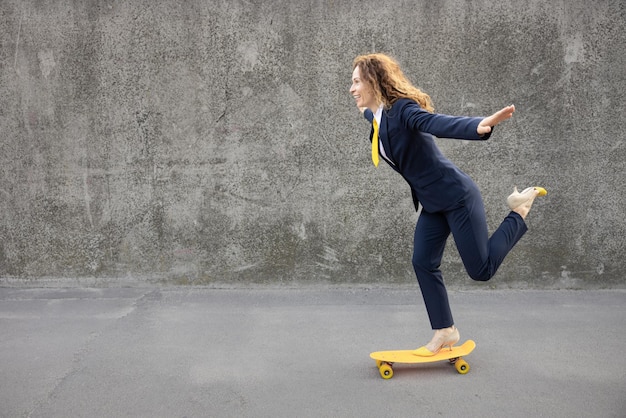 Heureuse femme d'affaires allant au travail Drôle jeune femme faisant du skateboard jaune en plein air Retour au démarrage du travail et concept d'idée d'entreprise