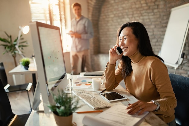 Heureuse femme d'affaires asiatique travaillant sur un ordinateur et parlant au téléphone au bureau