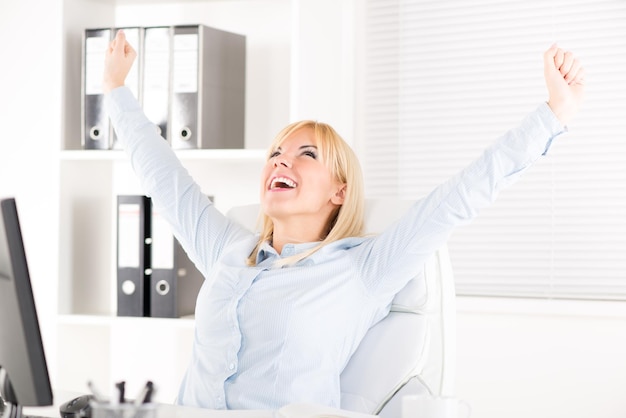 Heureuse femme d'affaires au bureau avec les bras levés.