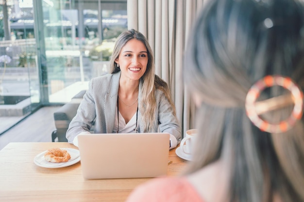 Heureuse femme d'affaires du millénaire utilisant un ordinateur portable et ayant un entretien avec une autre femme sur le lieu de travail